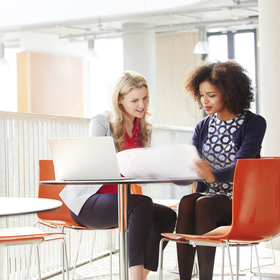 Two women sitting on red chairs looking over business plans