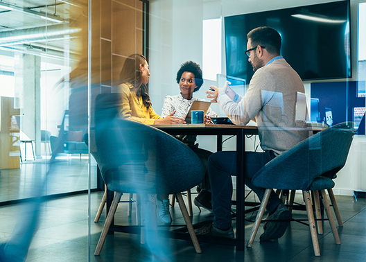 3 people having a meeting in a conference room with blurry silhouette of a person walking