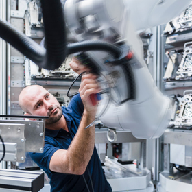 Homme travaillant sur un robot industriel dans une usine moderne.