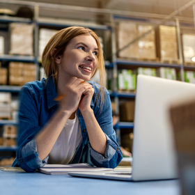 Young woman working in a warehouse on a laptop.