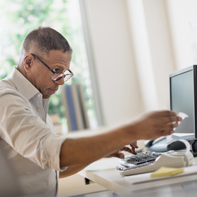 Man on computer looking at a receipt coming out of a calculator.